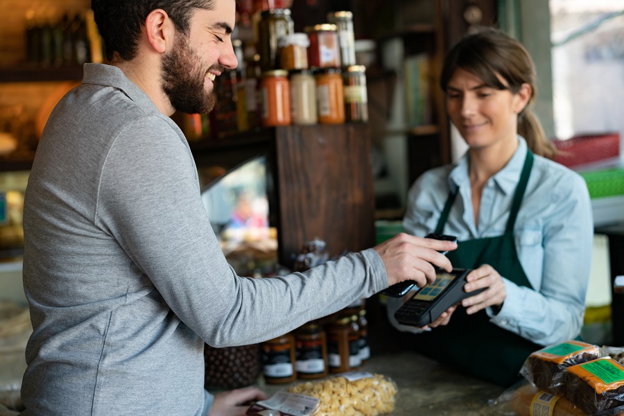 Handsome male customer at a delicatessen buying products making a contactless payment with smartphone - Small business concepts